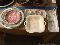 Multiple ceramic and porcelain serving items laid out on table showing Staffordshire red transferware bowl, white ceramic bowl, and various platters.