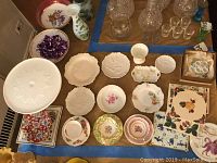Overview of the collection showing tea cups with saucers, various plates, a milk glass cake stand, and candle holder box.