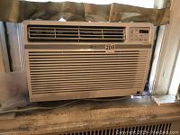 LG window air conditioner installed in a window, showing the front grille with air vents and control panel on the right.