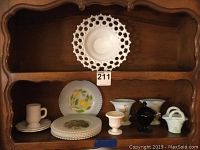 Wide view of shelf display showing all lot items including Victorian milk glass plates, painted decorative plates, slag glass vases, black candy jar and mint green basket dish