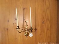 Pair of brass candle sconces mounted on wood wall, each holding two white taper candles.