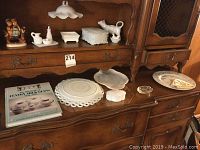 Full view of wooden cabinet displaying various milk glass items including platters, trinket boxes, cow creamer, Jewish platter, and Fenton Glass catalog.