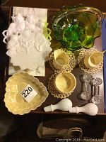 Lot overview including milk glass plates with animal motifs, green glass basket, cream-colored decorative dishes, bottle stoppers, and crystal spoon holders arranged on wooden table.