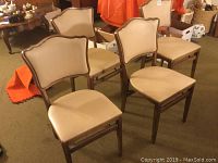 Four beige upholstered Stakmore folding chairs with wooden frames arranged on carpet.