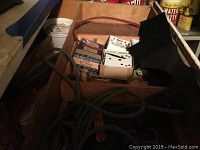 Wooden box containing assorted hardware boxes, coiled electrical cords, and miscellaneous tools.