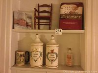 Full view of all items on shelf: two ceramic containers, ceramic mug, small wooden chair, dictionary book, and baby book.