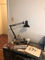 Full desk view with black boom lamp on, marble pencil holders, apothecary jar, and office supplies spread on glass-top table.