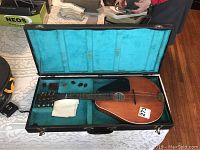 Mandolin placed inside open black hard case with turquoise lining on table, shows instrument and case