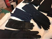 Photo of several pairs of women's gloves including black, navy, and blue cloth and leather gloves neatly laid out on a white surface.