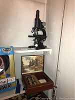 Ornate wooden box with interior painting and three brass-like cylindrical instruments and small accessories.