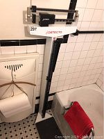 Full view of Detecto mechanical physician scale placed in bathroom near bathtub and tile wall. Visible height rod attached to upright column and black standing platform.