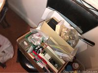 Box of assorted sewing buttons, notions, and accessories on a chair.