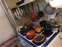 Wide view of kitchen stove area showing multiple pots and pans including cast iron cookware, enamelware, and utensils hanging on wall