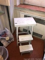 Front view of white painted wooden step stool showing two steps and top platform, with worn paint and scratches.