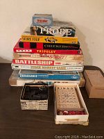Stack of vintage board game boxes including Probe, Score Four, Checkers, Tripoley, Sorry!, Battleship, Stock Market, and Renaissance chessmen, with dominoes and bingo game pieces in front.