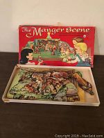 Top-down photo of original box labeled 'The Manger Scene' showing vintage illustration of children and nativity scene with cutout paper pieces inside.
