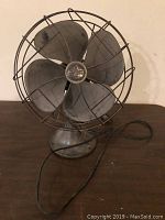 Front view of vintage Emerson electric fan showing four metal blades and wire protective cage