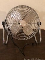 Front view of vintage metal table fan showing the cage, blades, and adjustable tilt stands with power cord.