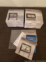 Two Garmin nüvi GPS devices in original boxes with accompanying manuals and accessory guides spread on a table.
