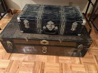 Photo of the vintage steamer trunk and navy blue metal carrying case stacked on wooden floor.