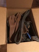 Top view of the box with brown rubber gloves and worn leather straps inside the box.