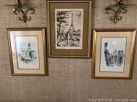 Three framed artworks hung on a wall: two watercolor prints on left and right, one original watercolor painting in center. All frames gold-toned and matted, glass covered.