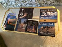 Top view of 8 books laid out on a gold and glass tray showing various titles and covers including Great Plains and Lewis & Clark.
