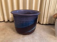 Angled side view of the round pottery planter showing blue and brown exterior glaze and wide rim.