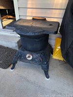 Full front angle view of antique cast iron water heater stove showing round stove lids, ornate base, and legs.