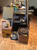 Full view of the batch showing the projector box, carrying cases, reels, and projection screen in a room with wooden flooring