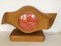 Front view of the vintage wooden airplane propeller clock showing the red clock face with white numbers and the wood grain.