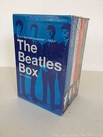 Front and front angled view showing the sealed Beatles Box with blue cover and the title 'The Beatles Box' by Alan Clayson, including image of the Beatles.