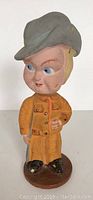 Front view of vintage plaster bobblehead figurine showing orange outfit, gray hat, and detailed facial features.