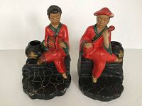 Front view of the two vintage plaster figures seated on black stone-like base with black pots.