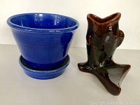 Brown fish-shaped pottery vase and blue ceramic planter pot with saucer seen from front angle