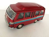 Left side view of red tin toy traveling car, showing overall shape, paint condition, and details including windows and wheels.