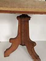 Close-up photo of the carved wooden base depicting a single central support with three curved legs