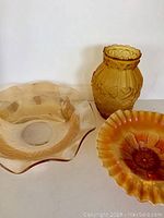 Three amber glass pieces including an Iris design bowl, a large wavy rim bowl, and a ribbed vase with scalloped rim.