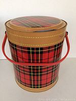 Full view of the vintage tin cooler showing plaid pattern, lid, and red handle