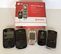 Five cellular phones displayed in front of an LG 240 Rogers box, showing two BlackBerry phones, one Nokia slider phone, one LG flip phone with camera lens, and one LG phone box.