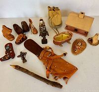 Photo showing entire collection of First Nations themed handcrafted items including leather moccasins, wooden figurines, small house, cradle, pouch, twig and decorative items.