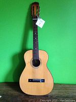 Front view of the 1960s Winston Parlour guitar showing its natural wood color top, six strings, slotted headstock with tuning pegs, and partial wear signs.