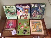 Front covers of six vintage children's books: Bambi, Cinderella, Peter Pan, Little Ballerina, Guinness Book of Records, The Royal Hiccups shown on a wooden table.