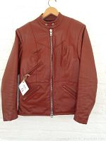 Front view of brown leather motorcycle cafe racer jacket hanging on hanger against white background, fully zipped.