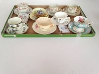 Tray with 8 assorted china tea cups and saucers with the Tea Time mini book placed together for lot overview.