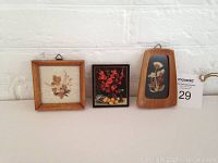 Front view of three floral-themed miniatures arranged against white brick wall, including two framed dried flower artworks and one floral plaque.