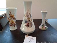 Front view of three flower-themed ceramic vases of different sizes and shapes on a dark surface with natural light from the side.