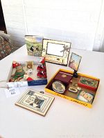 Overall view of lot contents including frames, book, pins, brooches, tins, paper weight, tape measure, thimble and Christmas decorations placed on table.