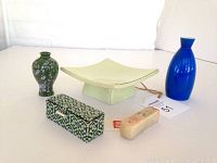 Photo of two oriental vases (green with white flowers and blue), ceramic platform dish, patterned box, and Chinese stone seal stamp on white surface with soda can for scale.