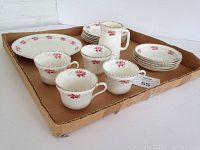 Photo showing 4 tea cups, 5 saucers, 6 smaller plates and 1 larger plate along with a milk pitcher with matching floral design, all arranged in a cardboard tray. Visible wear on pattern and trim noted.